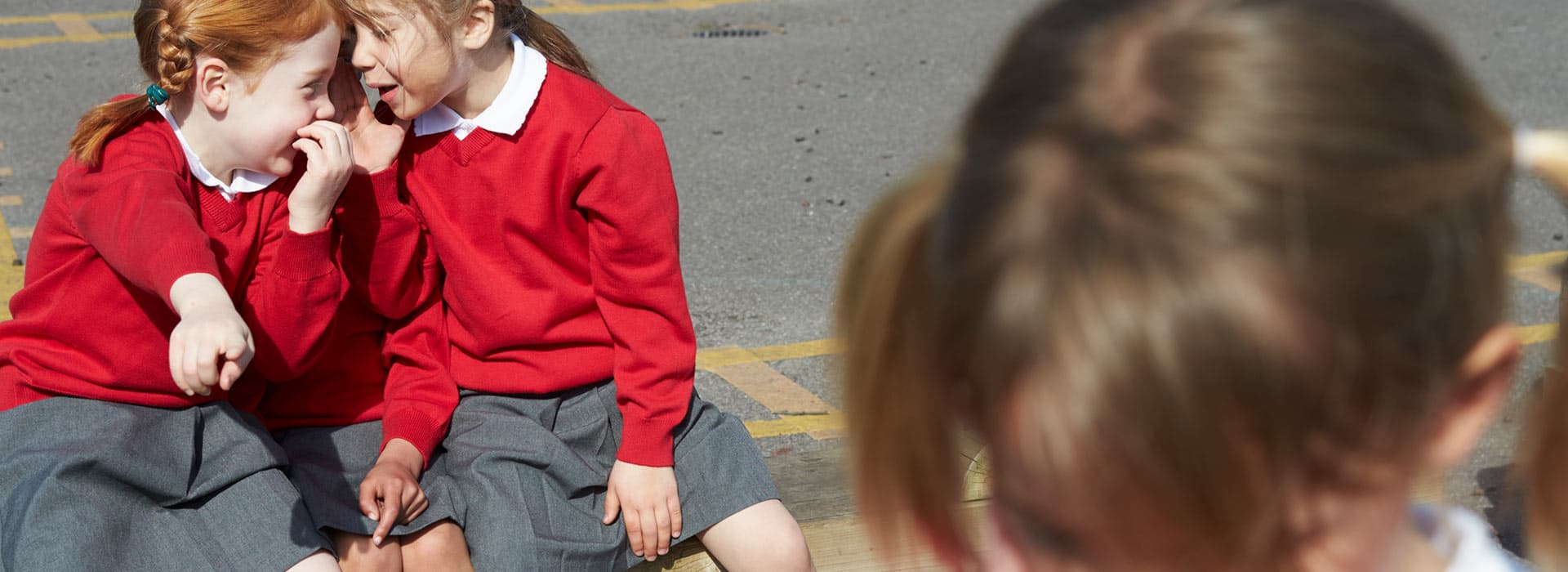 Two schoolgirls talking behind another schoolgirl's back