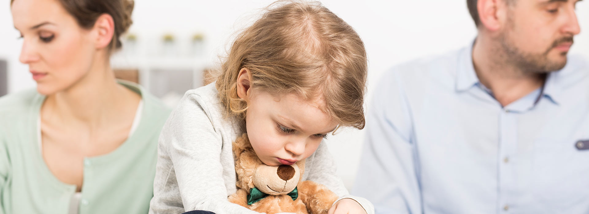 Sad girl cuddling a teddy bear because her parents are fighting